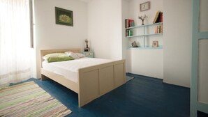 Un dormitorio con una cama, una mesita de noche, una estantería y un ventanal con cortinas.