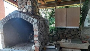 Cocina exterior de piedra con horno de pizza, un lavamanos y una pequeña mesa.
