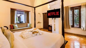 Un letto a baldacchino con un vassoio di cibo e bevande, una televisione che mostra 'NETFLIX' e vista sull'esterno attraverso una finestra.