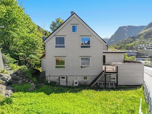Ein zweistöckiges Haus mit einem kleinen Balkon, einer Treppe, die zu der oberen Etage führt, und Blick auf eine gebirgige Landschaft.