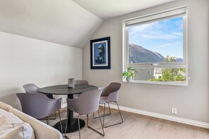 Ein Essbereich mit einem runden Tisch und vier Stühlen, einem gerahmten Kunstwerk an der Wand und einem Fenster mit Blick auf die Berge.