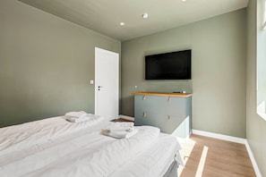 Ein Schlafzimmer mit zwei Betten, einem an der Wand befestigten Fernseher und einer Holzkommode.