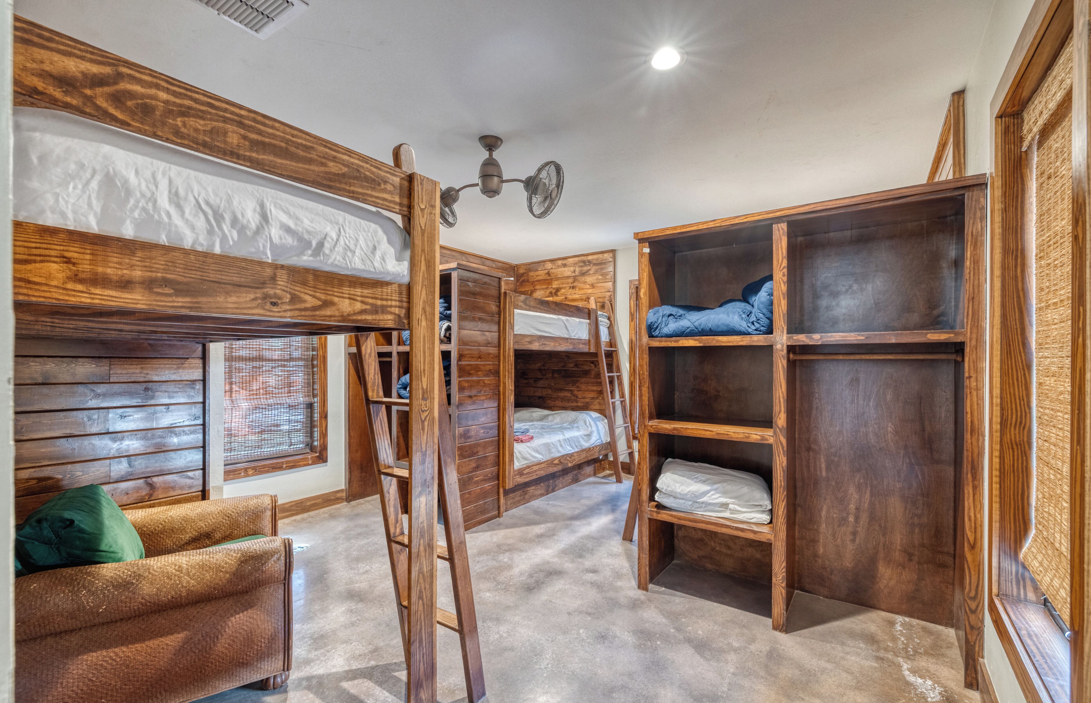 Une chambre avec un lit superposé, une échelle, des étagères en bois et un canapé.