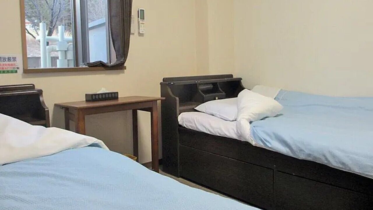 Habitación de hotel con dos camas, una mesita y un ventanal con cortinas.