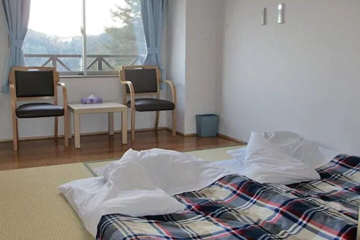 Ein Zimmer mit einem Bett, zwei Stühlen, einem kleinen Tisch und einem Fenster.