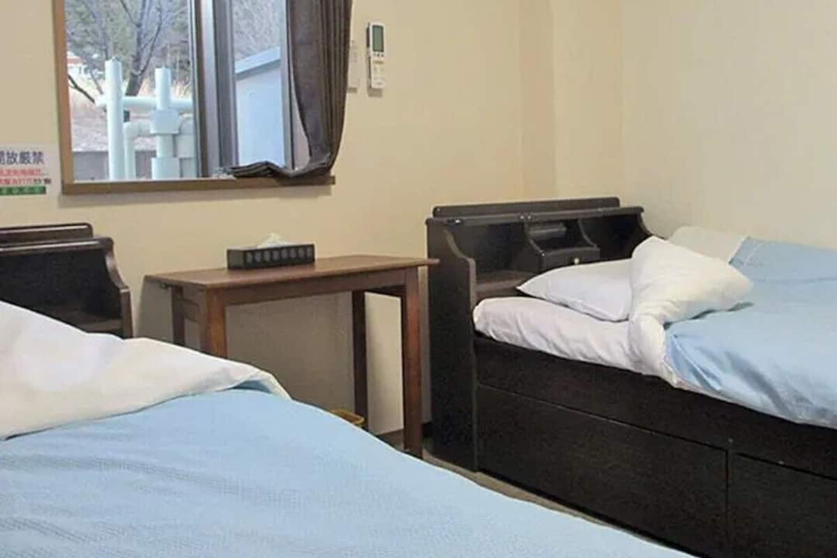 Ein Hotelzimmer mit zwei Einzelbetten, einem kleinen Tisch und einem Fenster mit Vorhängen.