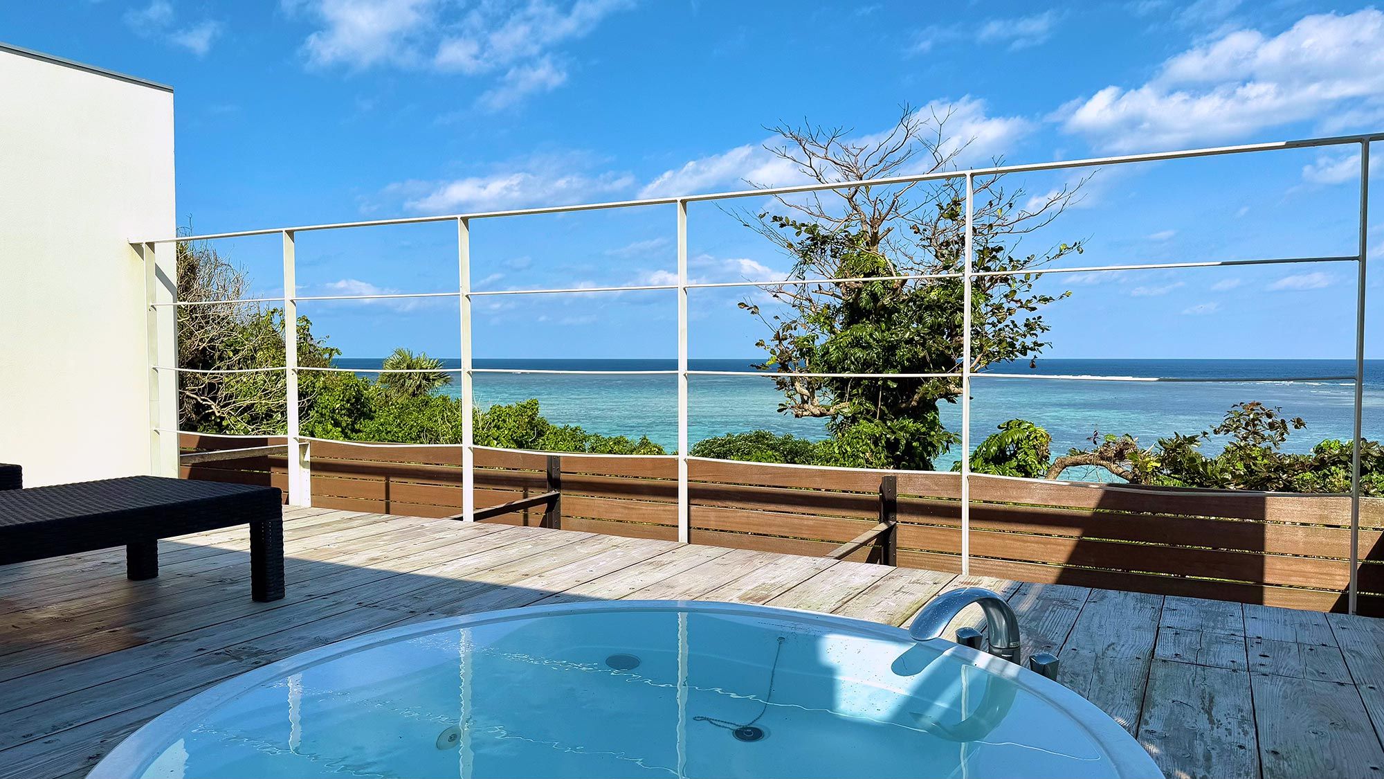 A wooden deck with a hot tub and a view of the ocean.