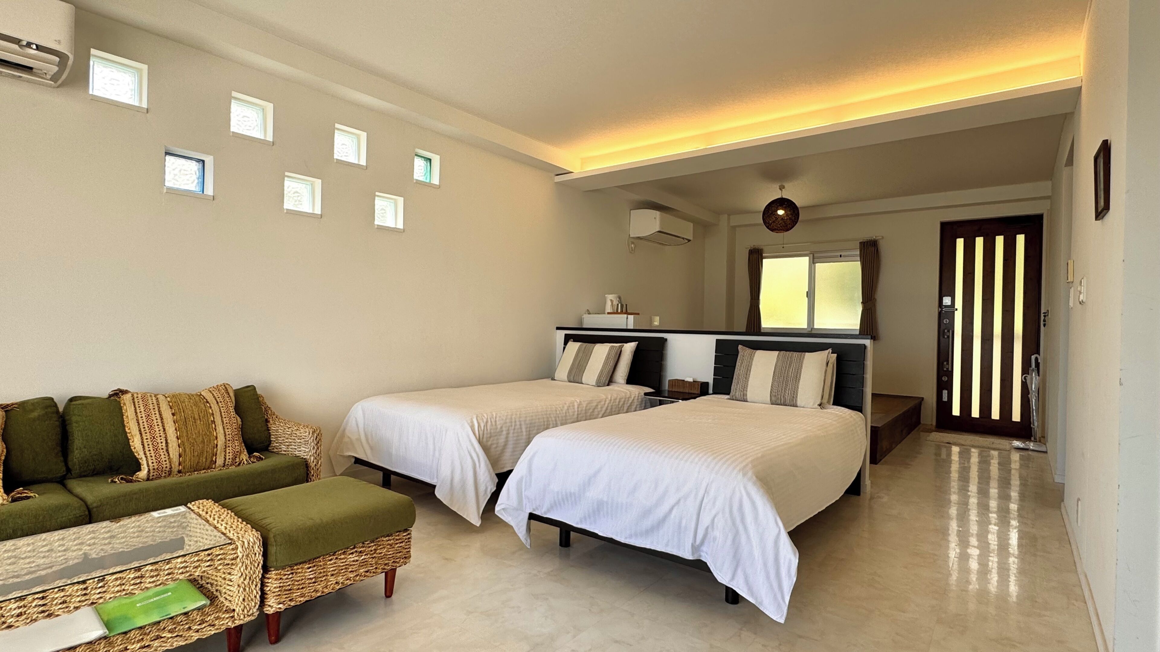 Habitación de hotel con dos camas, un sofá, una mesita y una ventana con cortinas.