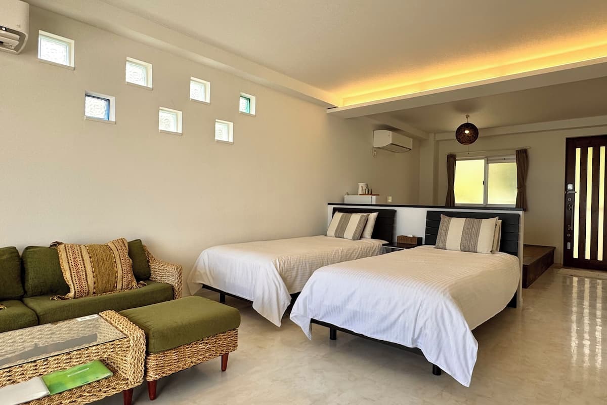 Habitación de hotel con dos camas, un sofá, una mesita y una ventana con cortinas.