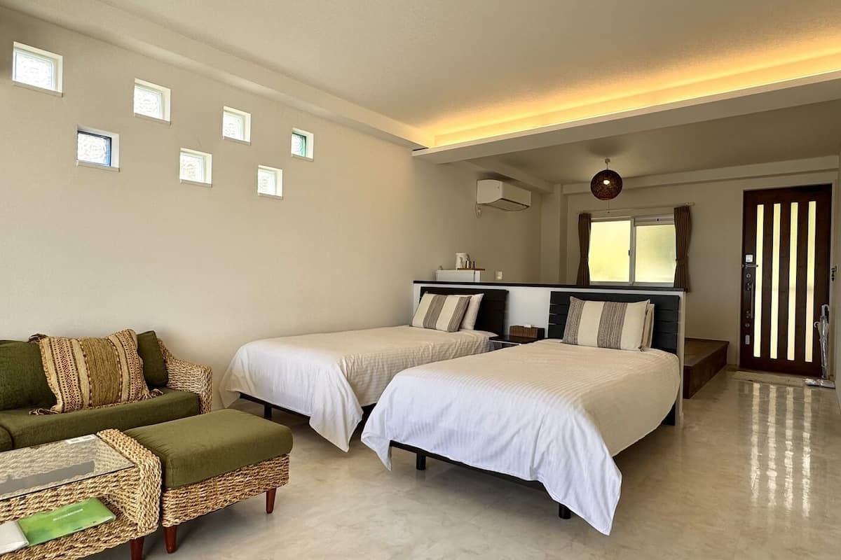 Una habitación de hotel con dos camas, un sofá, una mesita y una ventana con cortinas.