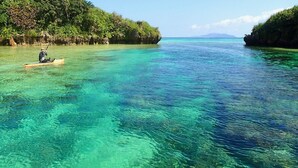 A kayaker on a clear turquoise sea with rocky islands and lush greenery in the background. - Island Village Ishigaki-jima (Ishigaki)