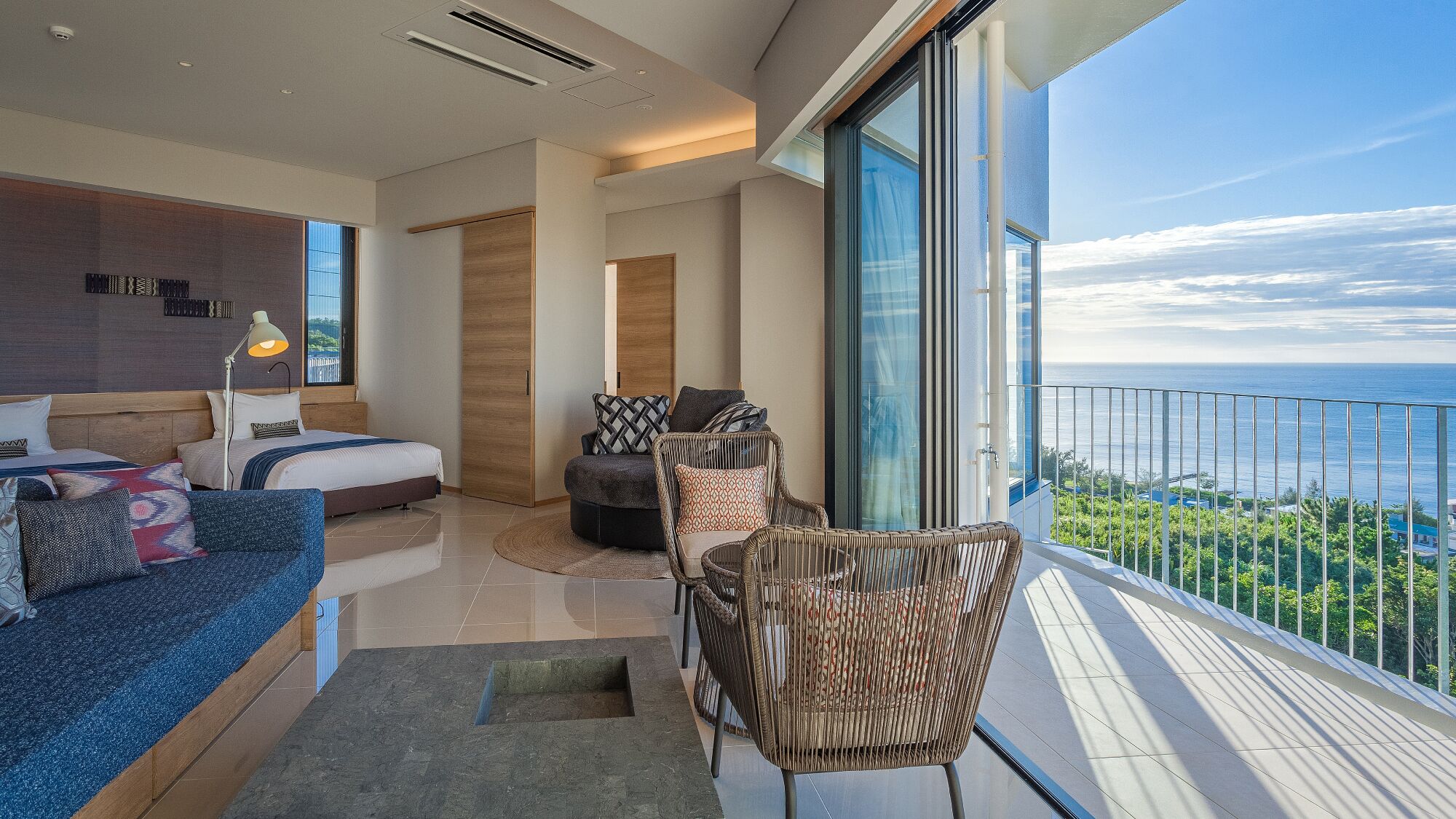 A modern bedroom with a large bed, a sofa, and a balcony with a view.