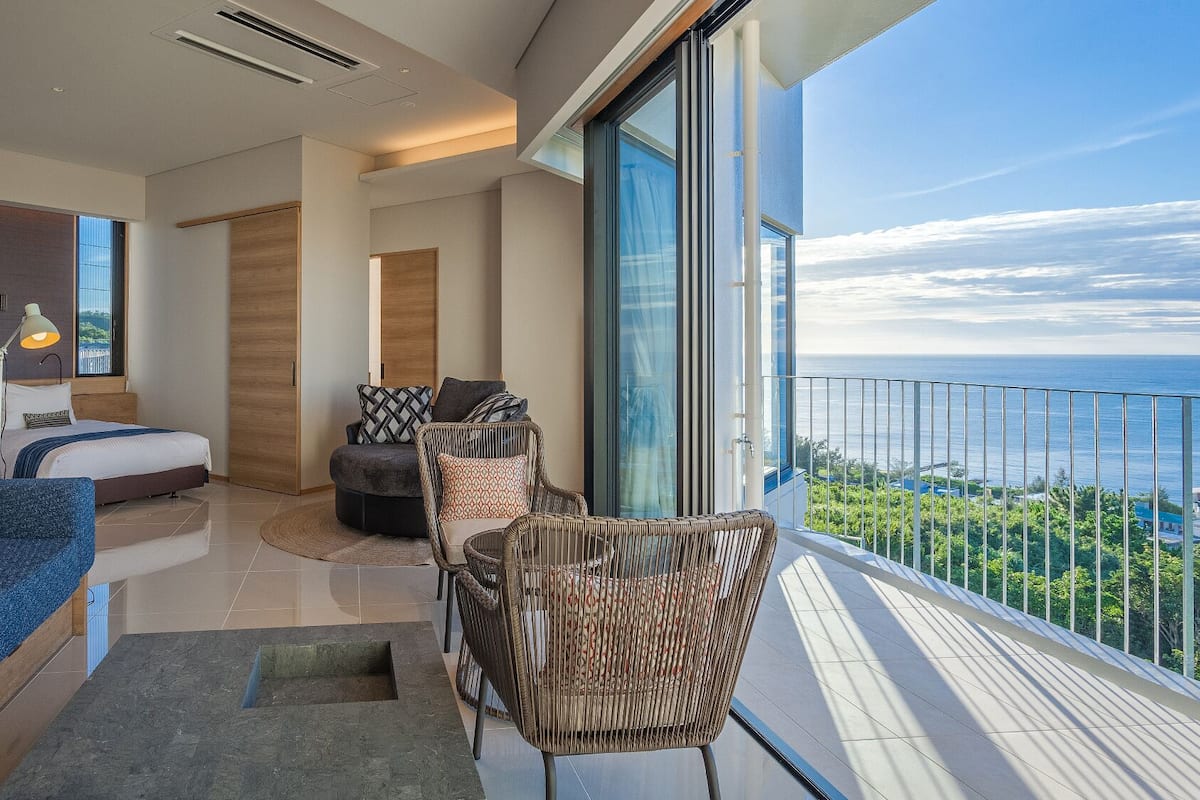 A modern bedroom with a large bed, a sofa, and a balcony with a view.