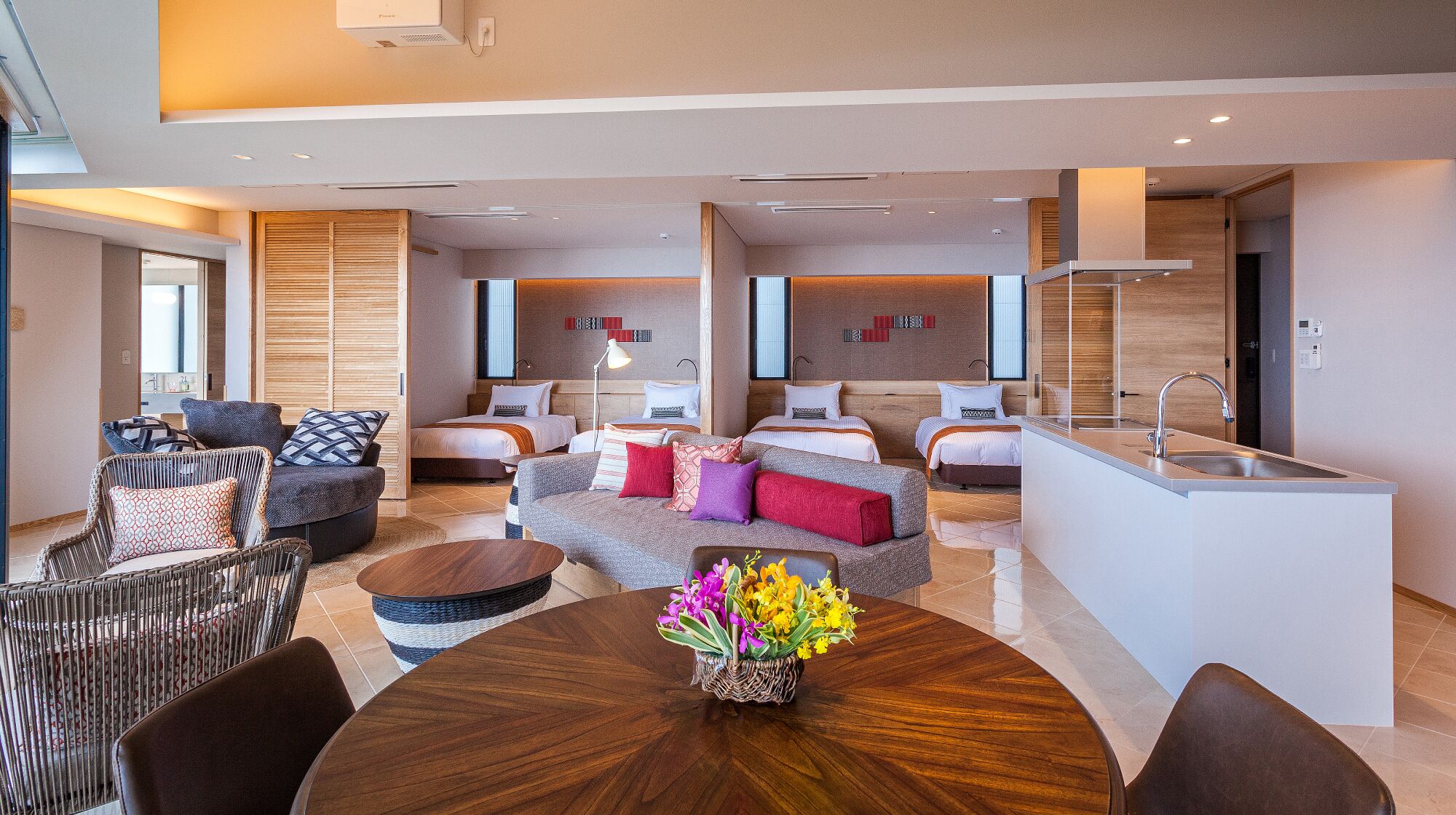 A modern hotel room with a dining area, two bedrooms, a kitchen, and a bathroom.