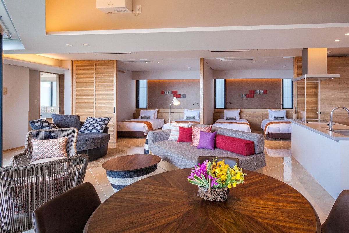 A modern hotel room with a dining area, two bedrooms, a kitchen, and a bathroom.