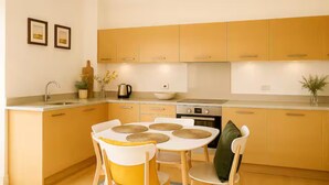 A compact kitchen with a dining table, chairs, and a coffee maker. - Chic 2BR in Shoreditch Prime Location (London)