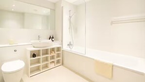 A modern bathroom with a white sink, mirror, and bathtub. - Chic 2BR in Shoreditch Prime Location (London)