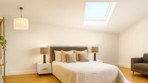 A bedroom with a large bed, two bedside tables, a lamp, a sofa, and a skylight. - Chic 2BR in Shoreditch Prime Location (London)