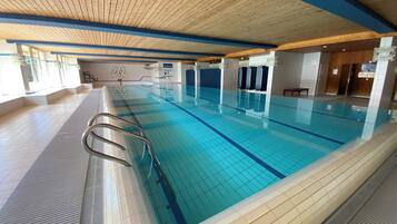 Une piscine intérieure à l’eau d’un bleu limpide, avec des murs carrelés et un plafond en bois.