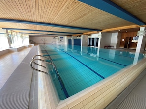 An indoor swimming pool with clear blue water, tiled walls, and a wooden ceiling.