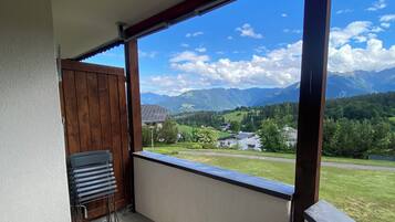 A balcony with a view of mountains, a wooden gate, and a stack of blue chairs.