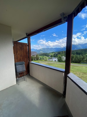 A balcony with a view of mountains, a wooden gate, and a stack of blue chairs.