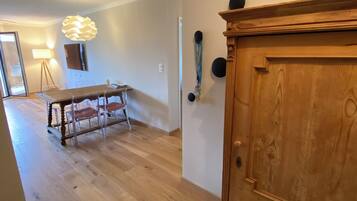 A room with a wooden floor, a dining table with chairs, a lamp, and a wooden cabinet.