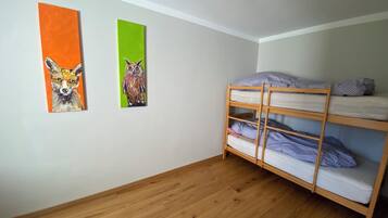 A room with a bunk bed, two paintings on the wall, and wooden flooring.