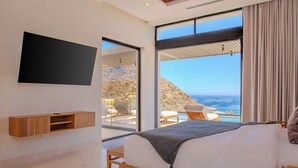 Een slaapkamer met een bed, een aan de muur bevestigde televisie en uitzicht op de oceaan.
