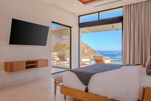 A bedroom with a bed, a TV mounted on the wall, and a view of the ocean. - Modern Cabo Ocean View Villa w/ Heated Pool, Hot Tub, Fire Pit & Luxury Design (Cabo San Lucas)