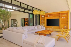 A modern living room with a sectional sofa, wooden coffee table, and built-in TV shelf. - Modern Cabo Ocean View Villa w/ Heated Pool, Hot Tub, Fire Pit & Luxury Design (Cabo San Lucas)