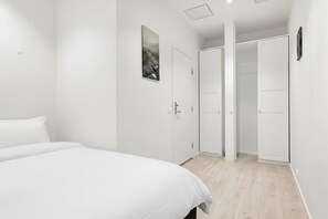 Une chambre à coucher avec un lit, des murs blancs, un plancher en bois et une porte donnant sur un placard.