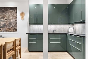 Une cuisine moderne avec des meubles de couleur verte, une table à manger en bois et un mur en pierre.