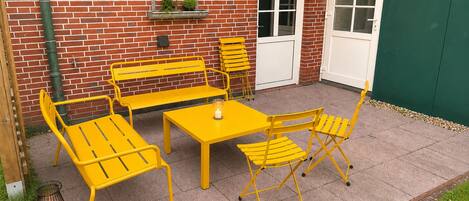 A patio with yellow metal furniture, a brick wall, a door, and a green wall.