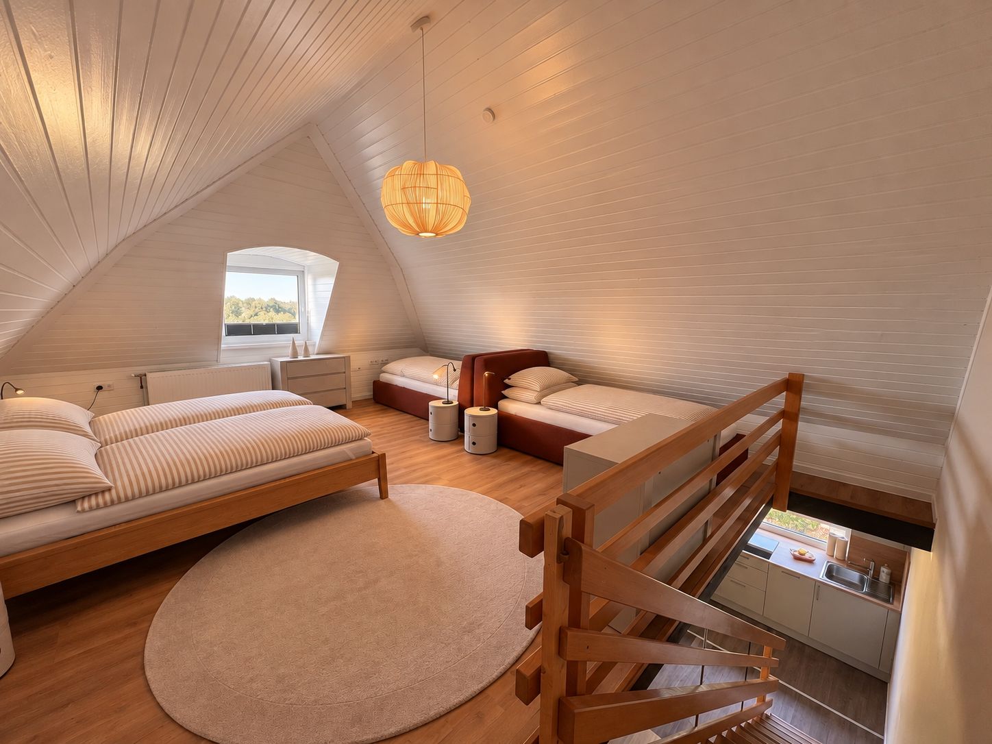 A modern loft bedroom with a sloped ceiling, a wooden bed frame, a round rug, a small bedside table, and a hanging light fixture.