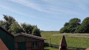 A balcony with a wooden table and chairs, a small brick building, and a grassy field with wind turbines in the background. - elf-36 (Esens)