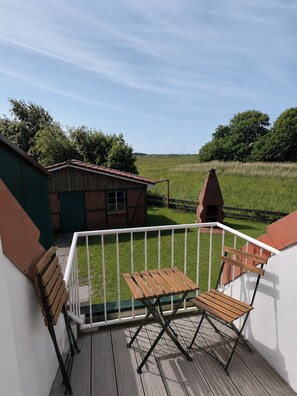 Un balcone con tavolo e sedie in legno, un piccolo edificio in mattoni e un campo erboso con turbine eoliche sullo sfondo.