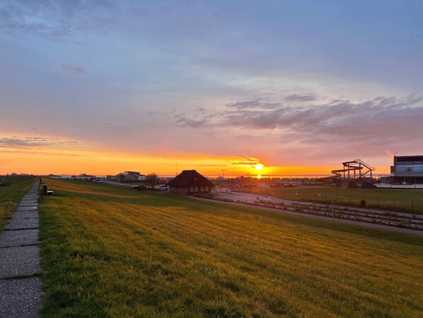 Tramonto su un prato con un sentiero lastricato e edifici industriali sullo sfondo.