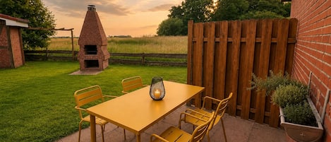 Un patio con una barbacoa de ladrillo, una mesa de madera y sillas.