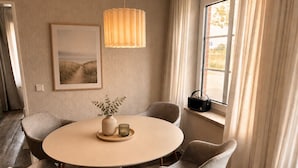 Et rundt spisebord med seks stole, en vase med en plante, et indrammet billede på væggen og en radio på vindueskarmen.