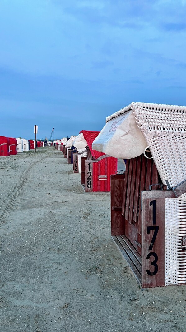 Une rangée de cabanes de plage numérotées 172, 173 et 128, avec un sentier sablonneux menant à la plage.