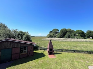 A rural landscape with a small brick building and a conical structure, surrounded by fields and trees.
