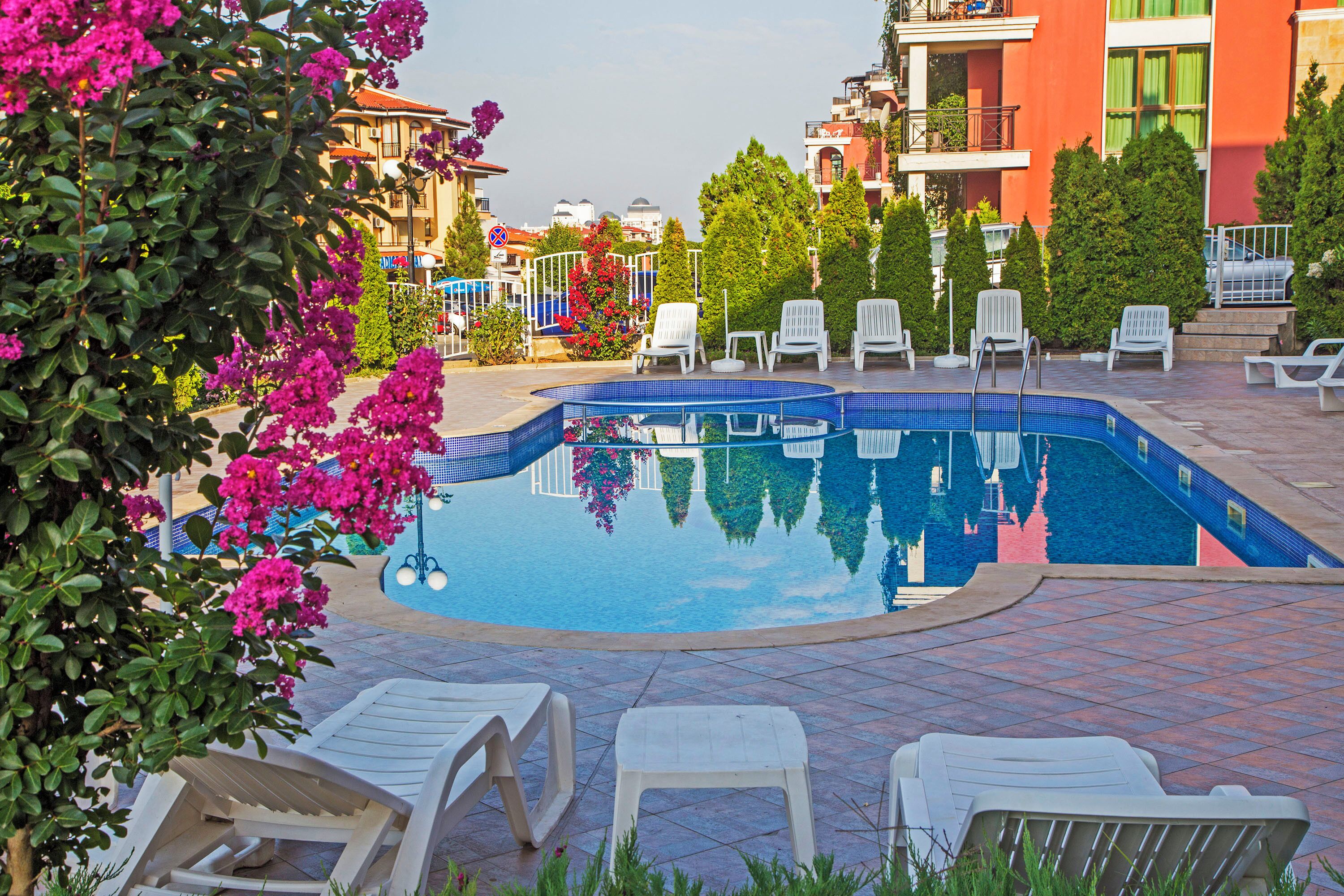 A swimming pool with lounge chairs, surrounded by buildings and greenery.