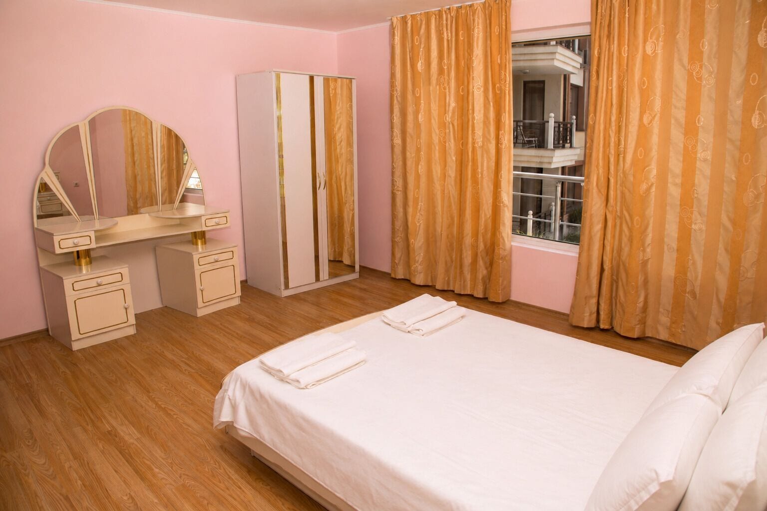 Una habitación de hotel con cama, tocador con espejo, armario y ventana con cortinas.