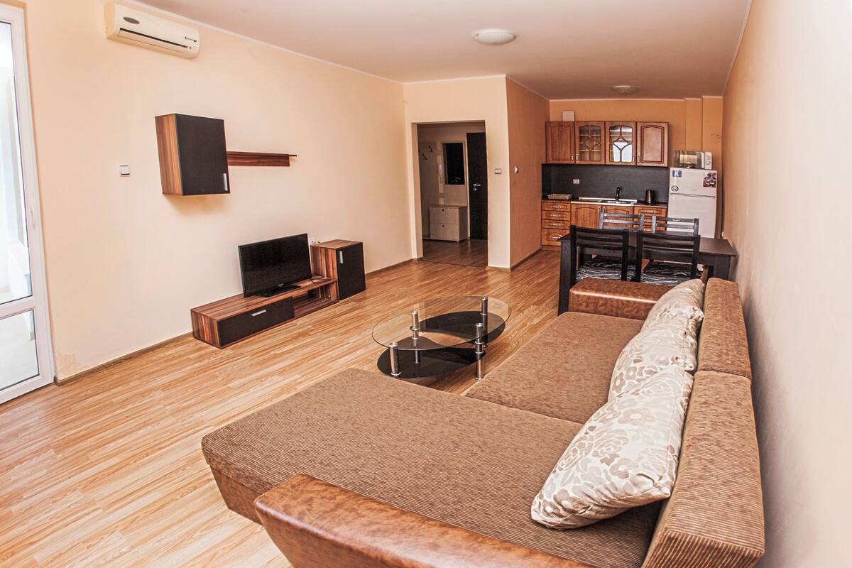 A living room with a sofa, TV, and a kitchen in the background.