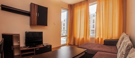 A living room with a sofa, a TV, a wooden cabinet, and a window with curtains.