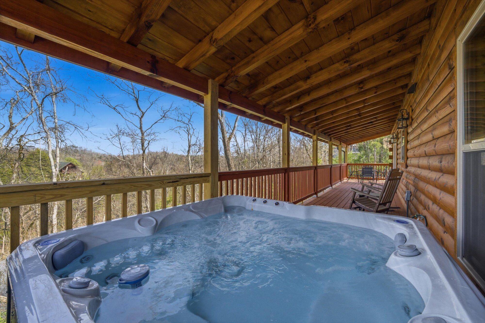 A wooden deck with a hot tub, wooden railings, and a view of trees and hills.