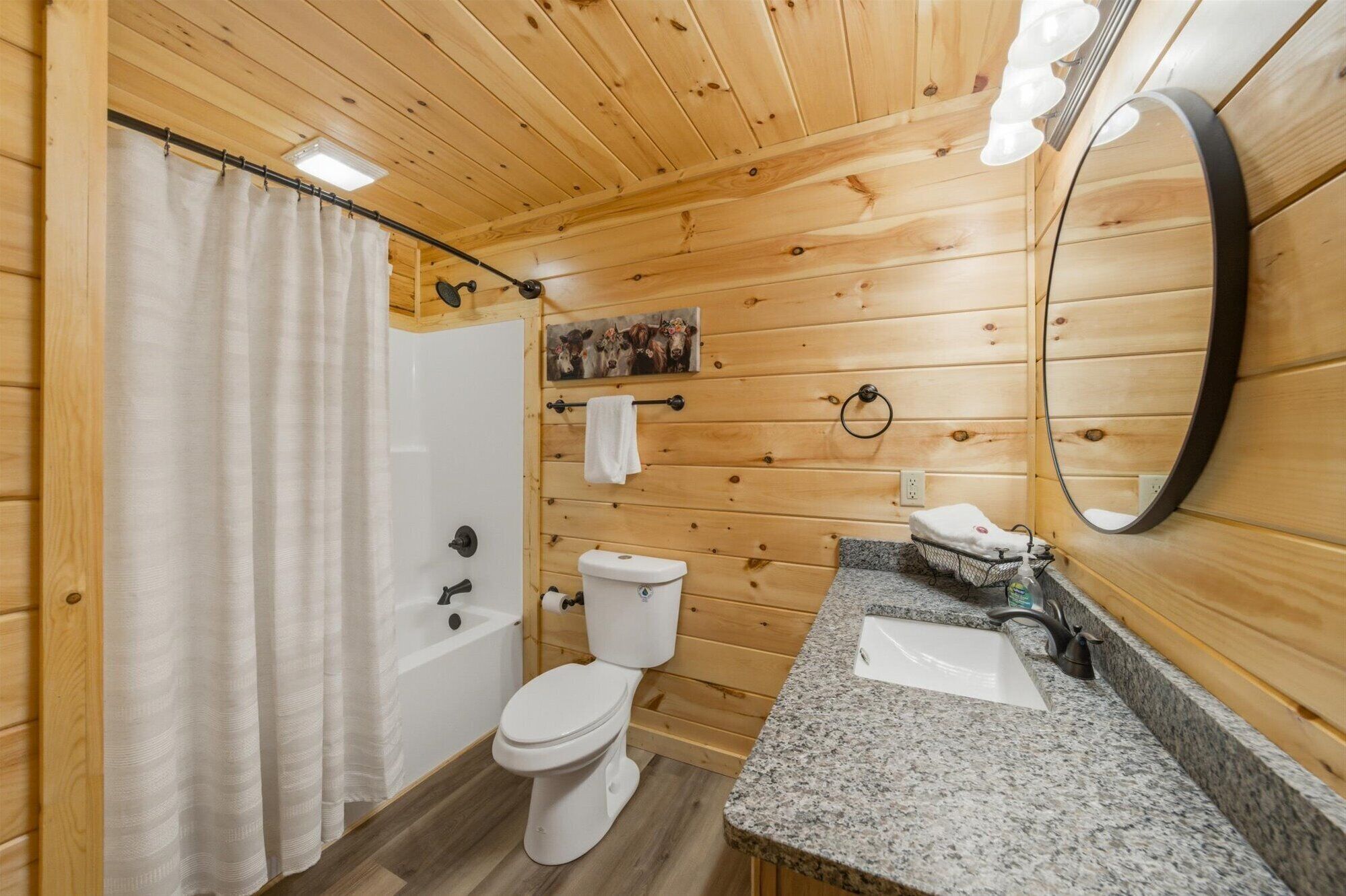 Une salle de bain rustique, aménagée dans une cabane en bois, comprenant une douche, des toilettes, un lavabo et un miroir.