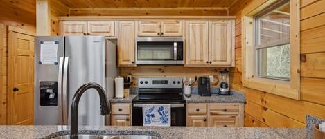 A kitchen with wooden cabinets, a stainless steel refrigerator, a microwave, an oven, a sink, granite countertops, and a window.