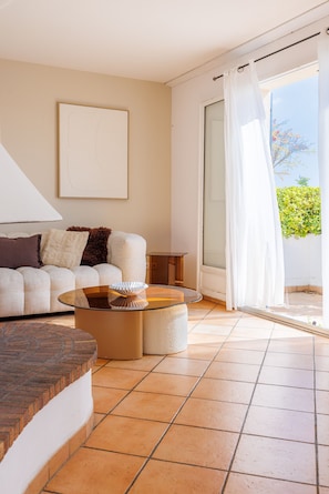 A modern living room with a sofa, a glass coffee table, and a sliding glass door leading to an outdoor area. - La Cabanette – Villa with pool and seaview (Tourrettes-sur-Loup)